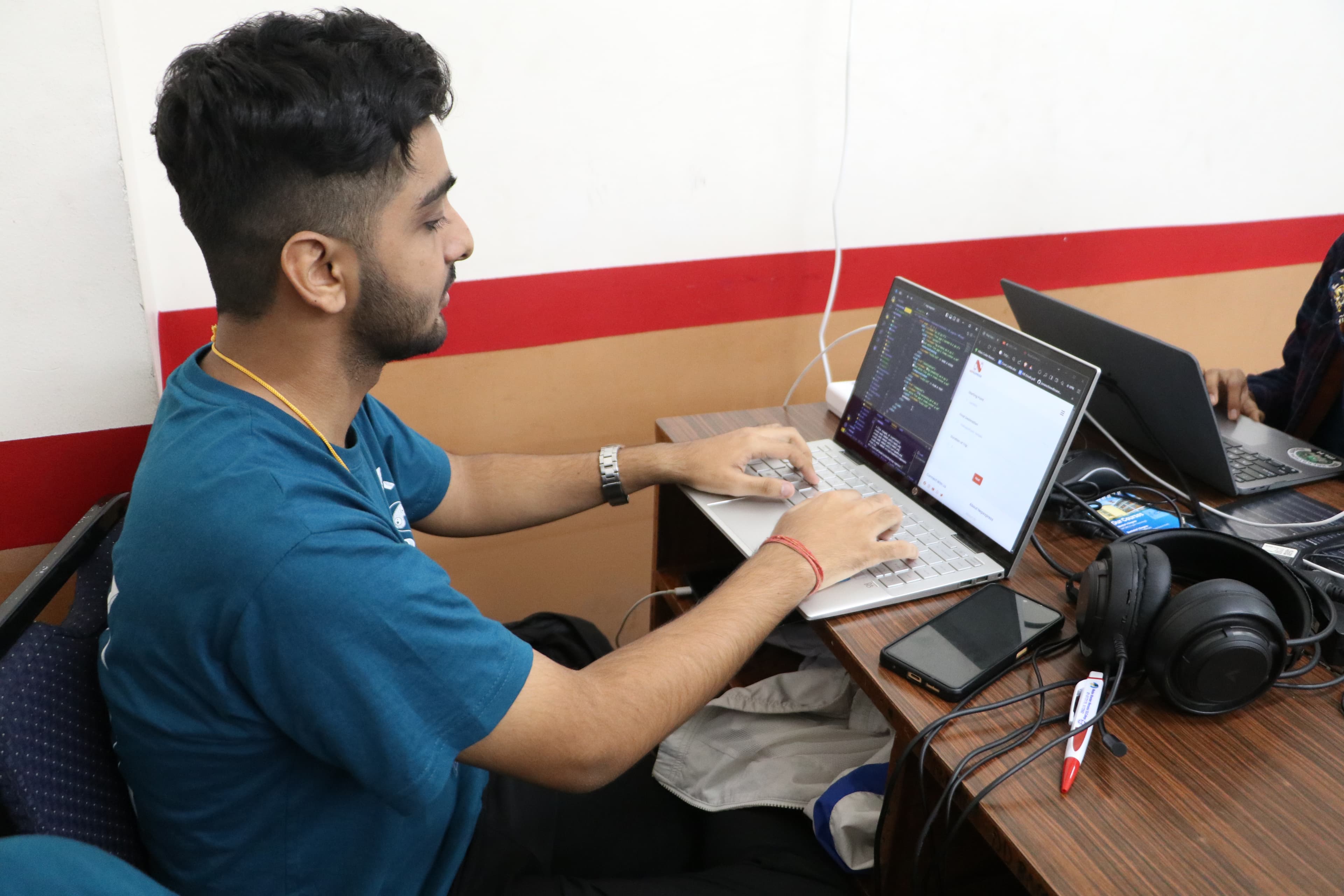 Sanchit Pandey coding on a laptop at a desk while others work alongside him